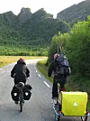 To syklister med bagasje på landevei omgitt av grønne fjell