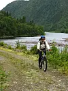 Syklist med hjelm på grusvei ved elv i grønn dal