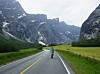 Syklist på landevei omgitt av høye fjell og grønne dalenger