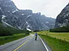 Syklist på landevei omgitt av høye fjell og grønne dalenger