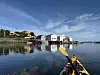 Gul kajakk i forgrunnen med hvite sjøhus og brygge speilet i rolig vann.