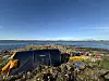 Blått telt ved steinete kyst med utstyr langs vannet og klar blå himmel.