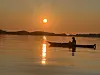 Silhuett av en person i båt på stille vann med reflektert solnedgang.