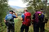 Fire personer med tursekker står ved et utsiktspunkt i skogen og ser mot fjell og dal.
