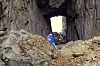 Person i blå og rosa klær sitter på steiner inne i en grotte med lys åpning i bakgrunnen.