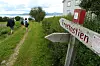 Turgåere går på en grussti ved kysten med et treskilt som viser Fostastjern i forgrunnen.